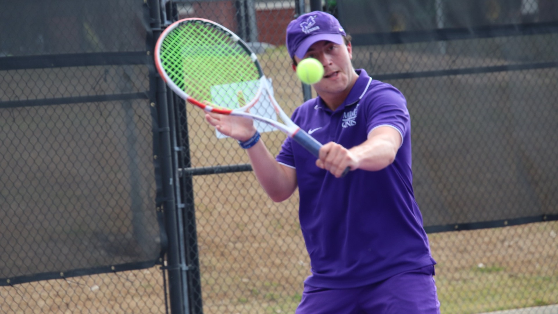 A man in a purple shirt and shorts engaged in a game of tennis.