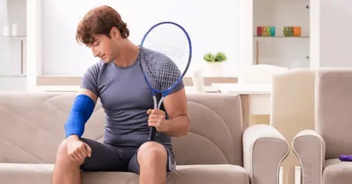 A man sitting on a couch with a tennis racket, ready for a game of tennis.